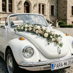 Biały kabriolet ozdobiony bukietem róż i eukaliptusa na masce, idealny przykład, jak udekorować samochód do ślubu. Białe wstążki dodają elegancji.