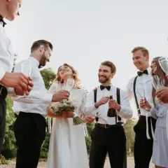 Świadek na weselu otwiera szampana, podczas gdy panna młoda i pan młody cieszą się chwilą z przyjaciółmi.
