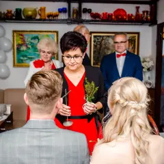 Kobieta udziela katolickie błogosławieństwo młodej parze, trzymając gałązkę i krzyż.