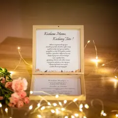 Drewniana szkatułka z listem od dzieci, zawierająca błogosławieństwo rodziców na ślub, ozdobiona kwiatami i światełkami.