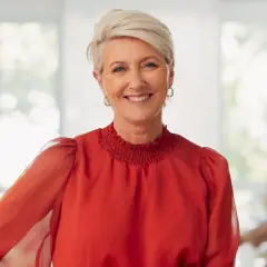 Uśmiechnięta kobieta z krótkimi blond włosami, w czerwonej bluzce. Idealna fryzura dla mamy weselnej, która chce wyglądać elegancko i nowocześnie.