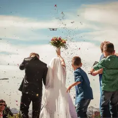 Radosne wyjście z kościoła pary młodej, obsypywanej konfetti. W tle dron filmuje uroczystość.