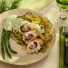 Menu weselne dania gorące: roladki z kurczaka ze szpinakiem i szynką, podane z zielonym makaronem, szparagami i kremowym sosem.