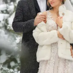 Para młoda w zimowej scenerii. Ona w białym futerku i koronkowej sukni, on w eleganckim płaszczu. Ich ślub w zimie wygląda bajkowo.