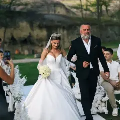 Ojciec prowadzi córkę do ołtarza, wypełniając zasady tradycji. Panna młoda w białej sukni i welonie, z bukietem róż, idzie u jego boku.