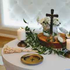 Stół na błogosławieństwo z krzyżem, świecami i bukietem białych kwiatów.