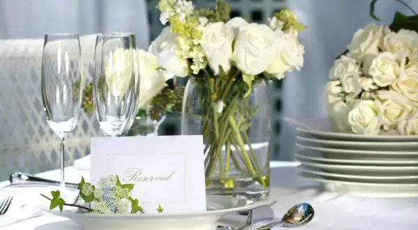 Elegancko nakryty stół z białymi różami, kieliszkami i kartą "Reserved". Idealny na przyjęcie, gdzie wedding planner cena jest kluczowa.