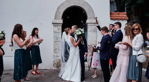 Para młoda całuje się przed kościołem, goście sypią bańki. To piękny ślub kościelny jednostronny.