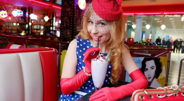 Kobieta w stylu pin up pije mleczny koktajl w retro restauracji.