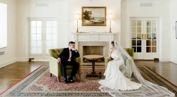 Para w eleganckich strojach siedzi naprzeciwko siebie, rozmawiając o tym, jak wziąć ślub cywilny.