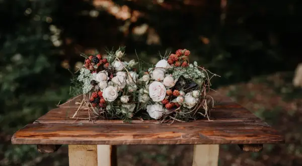Dwa bukiety ślubne boho z różami, jeżynami i gałązkami na drewnianym stole.