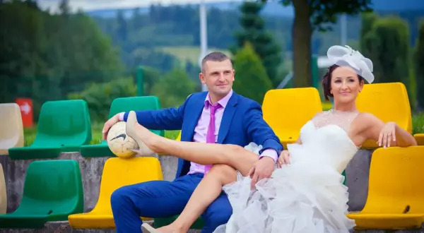 Para wykupiny panny młodej siedzi na trybunach. Pan młody trzyma piłkę, na której opiera nogę panny młodej.