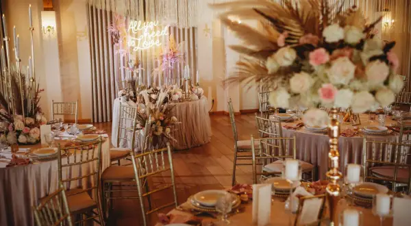 Elegancka sala weselna z neonem "All you need is love". Złote krzesła i pastelowe dekoracje. Zastanawiasz się, ile bierze dekoratorka na wesele?