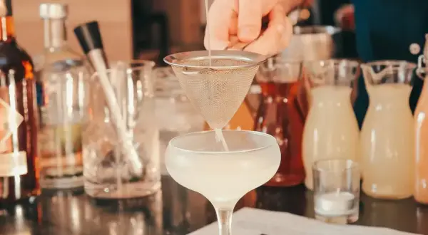 Barman przygotowuje drinka, obok stoją butelki z różnymi alkoholami i syropami. Idealny wybór, jaki alkohol na wesele, by zadowolić wszystkich gości.