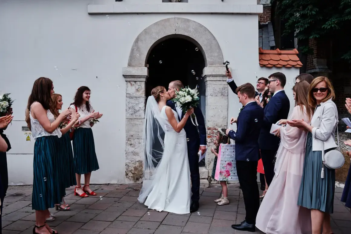 Para młoda całuje się przed kościołem, goście sypią bańki. To piękny ślub kościelny jednostronny.