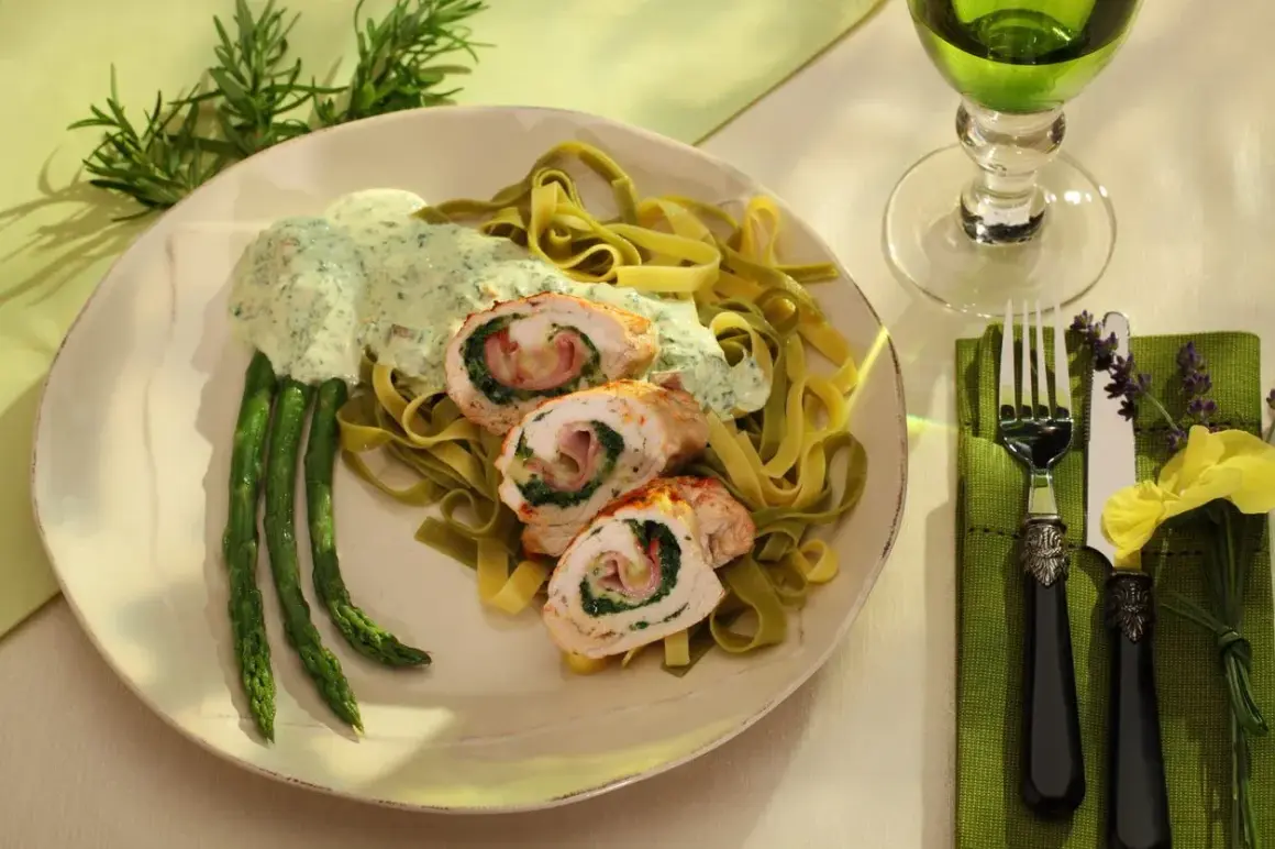 Menu weselne dania gorące: roladki z kurczaka ze szpinakiem i szynką, podane z zielonym makaronem, szparagami i kremowym sosem.