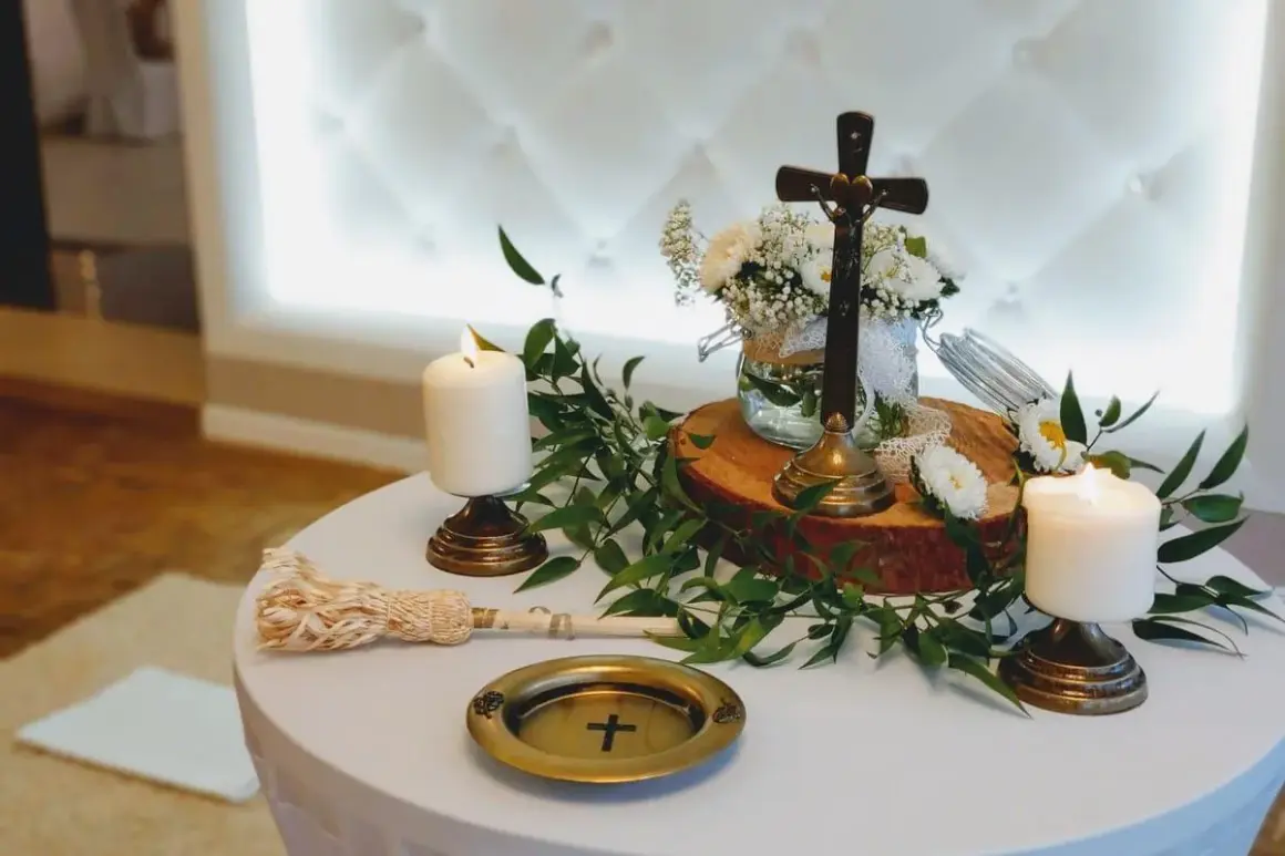 Stół na błogosławieństwo z krzyżem, świecami i bukietem białych kwiatów.