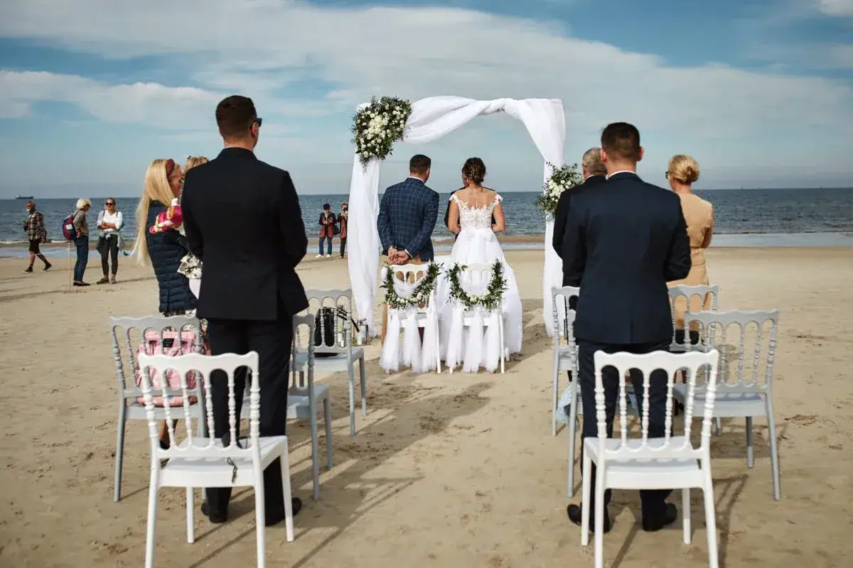 Piękny ślub na plaży w Polsce. Para młoda stoi przed ołtarzem, goście obserwują ceremonię.