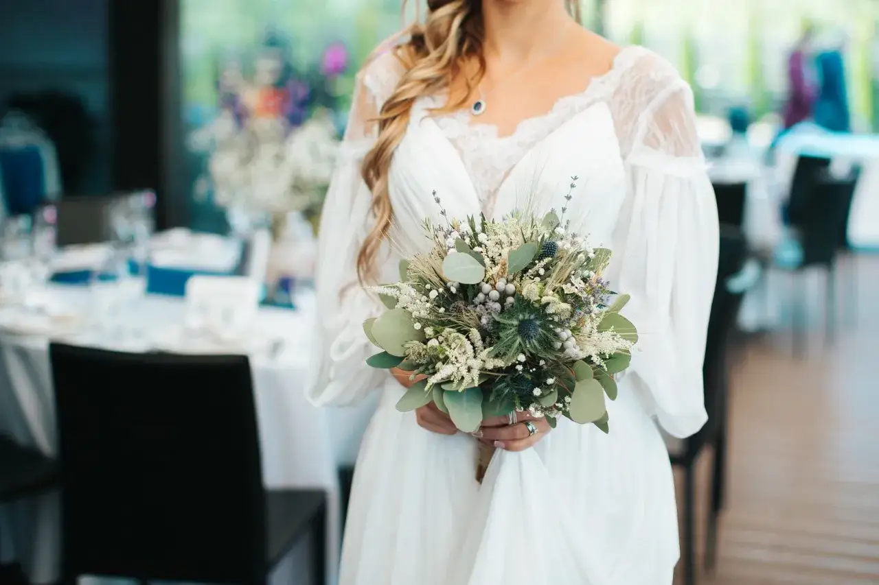Panna młoda w białej sukni trzyma bukiet ślubny boho z ostami, eukaliptusem i lawendą.