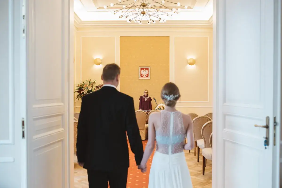 Para wchodzi do sali, by wziąć ślub cywilny. Urzędniczka czeka przy mównicy.