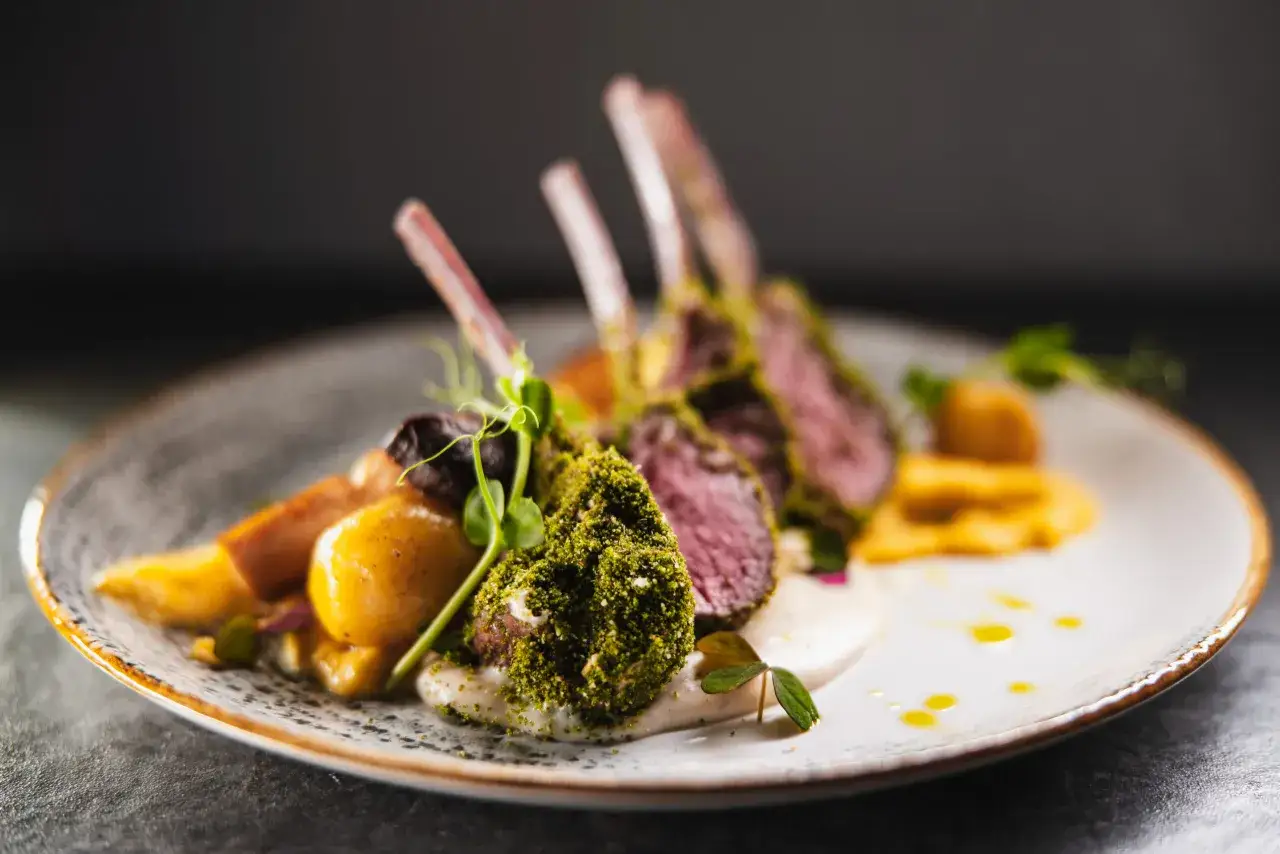 Eleganckie dania gorące z menu weselnego: pieczone kotleciki jagnięce w ziołach z puree i warzywami.