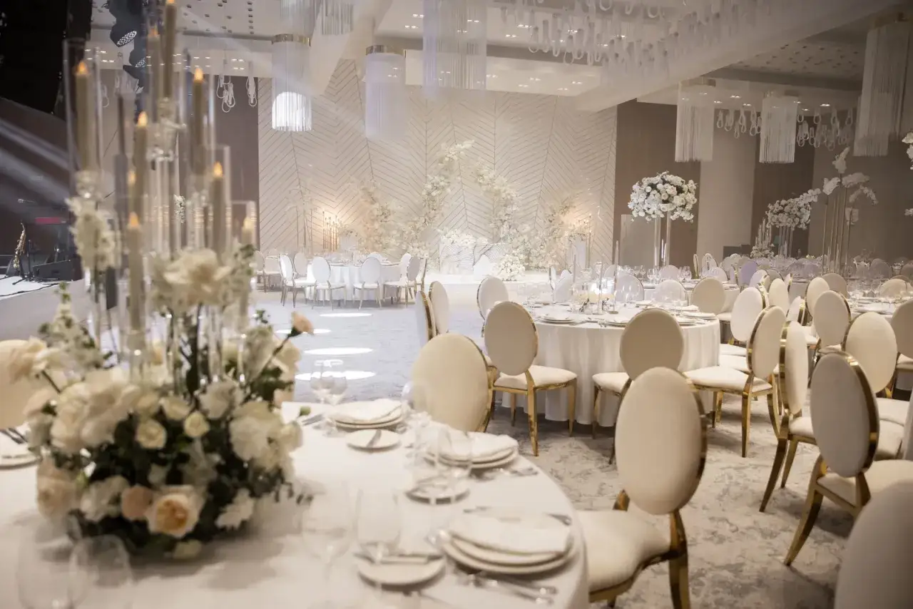 Elegancka sala weselna z białymi kwiatami i świecami. Stoły nakryte do uroczystej kolacji, gotowe na serwowanie wyśmienitych dań gorących z menu weselnego.