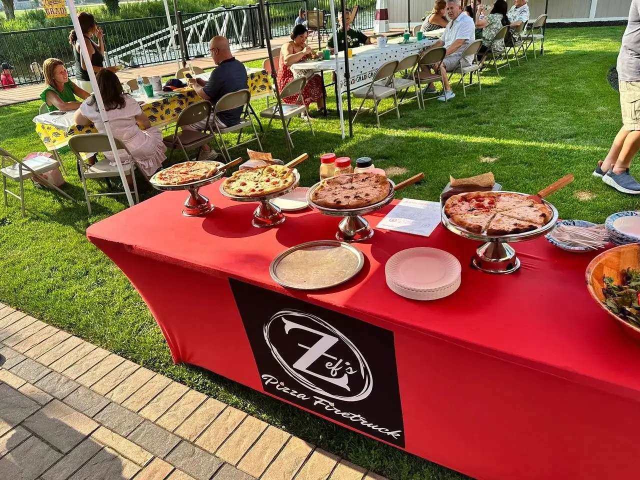 Stół z pizzą na weselu, goście siedzą przy stołach w tle.