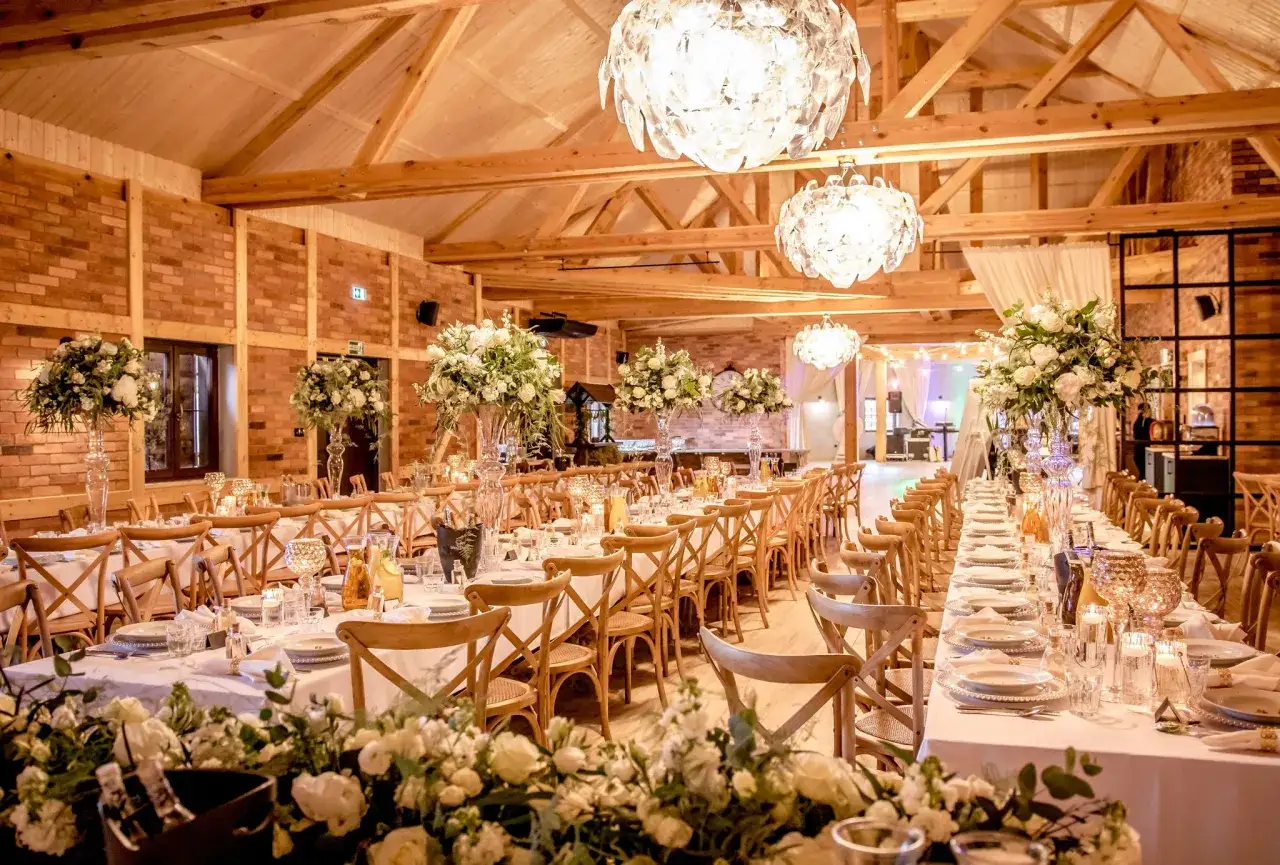 Elegancka sala weselna z długimi stołami, białymi kwiatami i kryształowymi żyrandolami. Idealne miejsce na przyjęcie, gdzie można zadać pytania do sali weselnej.