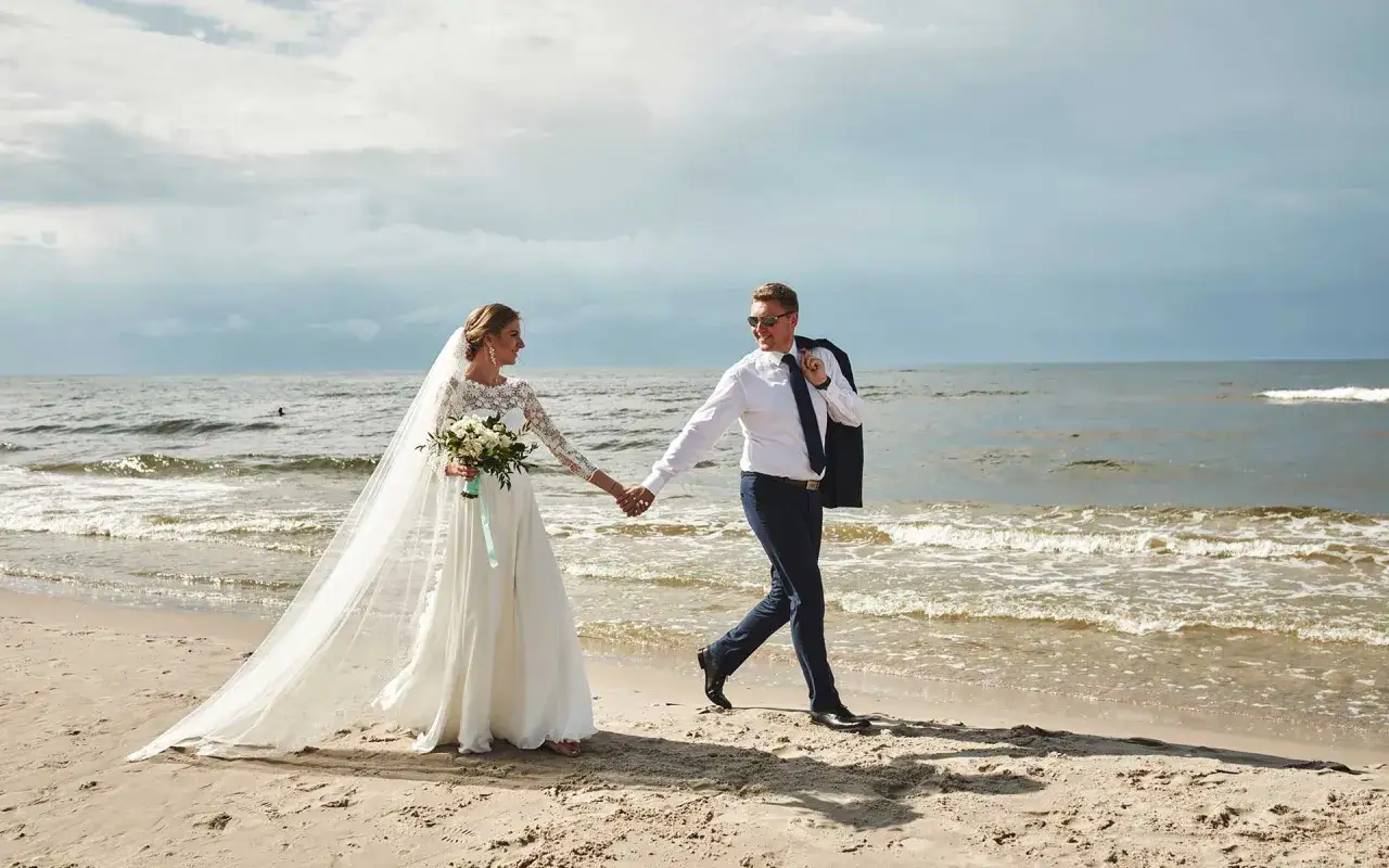 Szczęśliwa para podczas ślubu na plaży w Polsce. Panna młoda w sukni z welonem i bukietem, pan młody w garniturze.