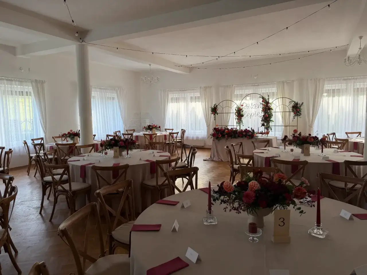 Elegancka sala weselna z okrągłymi stołami, kwiatami i numerami stołów. To idealna lista rzeczy na wesele, by stworzyć wyjątkową atmosferę.