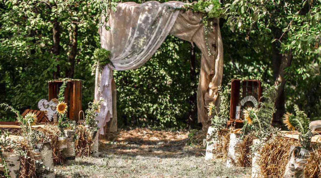 Udekorowany łuk z tkanin i zieleni, ozdobiony słonecznikami i drewnianymi skrzynkami. Idealne miejsce na ślub w plenerze boho.