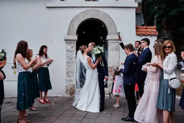 Para młoda całuje się przed kościołem, goście sypią bańki. To piękny ślub kościelny jednostronny.