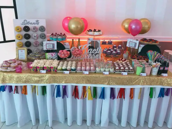 Słodki stół z donutami, babeczkami i deserami w słoiczkach, jak na wesele lata 80. Złoty obrus i kolorowe balony dodają blasku.