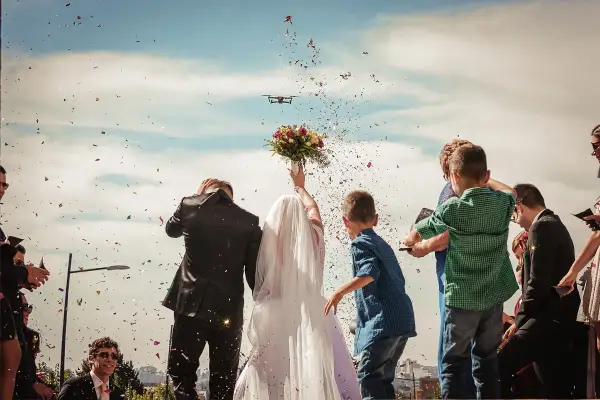 Radosne wyjście z kościoła pary młodej, obsypywanej konfetti. W tle dron filmuje uroczystość.