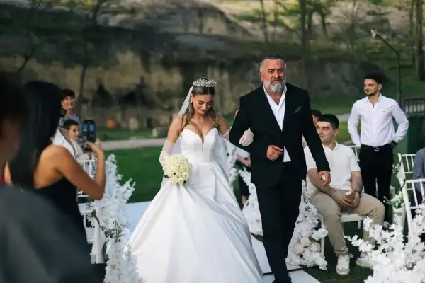 Ojciec prowadzi córkę do ołtarza, wypełniając zasady tradycji. Panna młoda w białej sukni i welonie, z bukietem róż, idzie u jego boku.