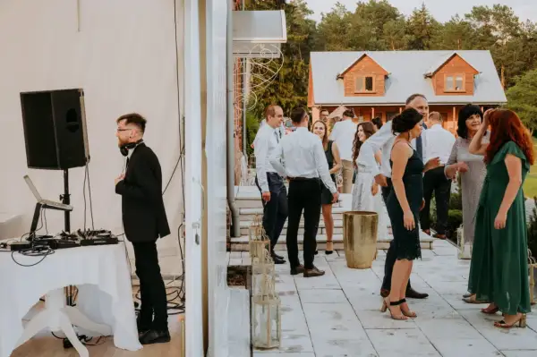 DJ przygotowuje się do przyjęcia weselnego w lesie. Goście bawią się na tarasie przed domem.